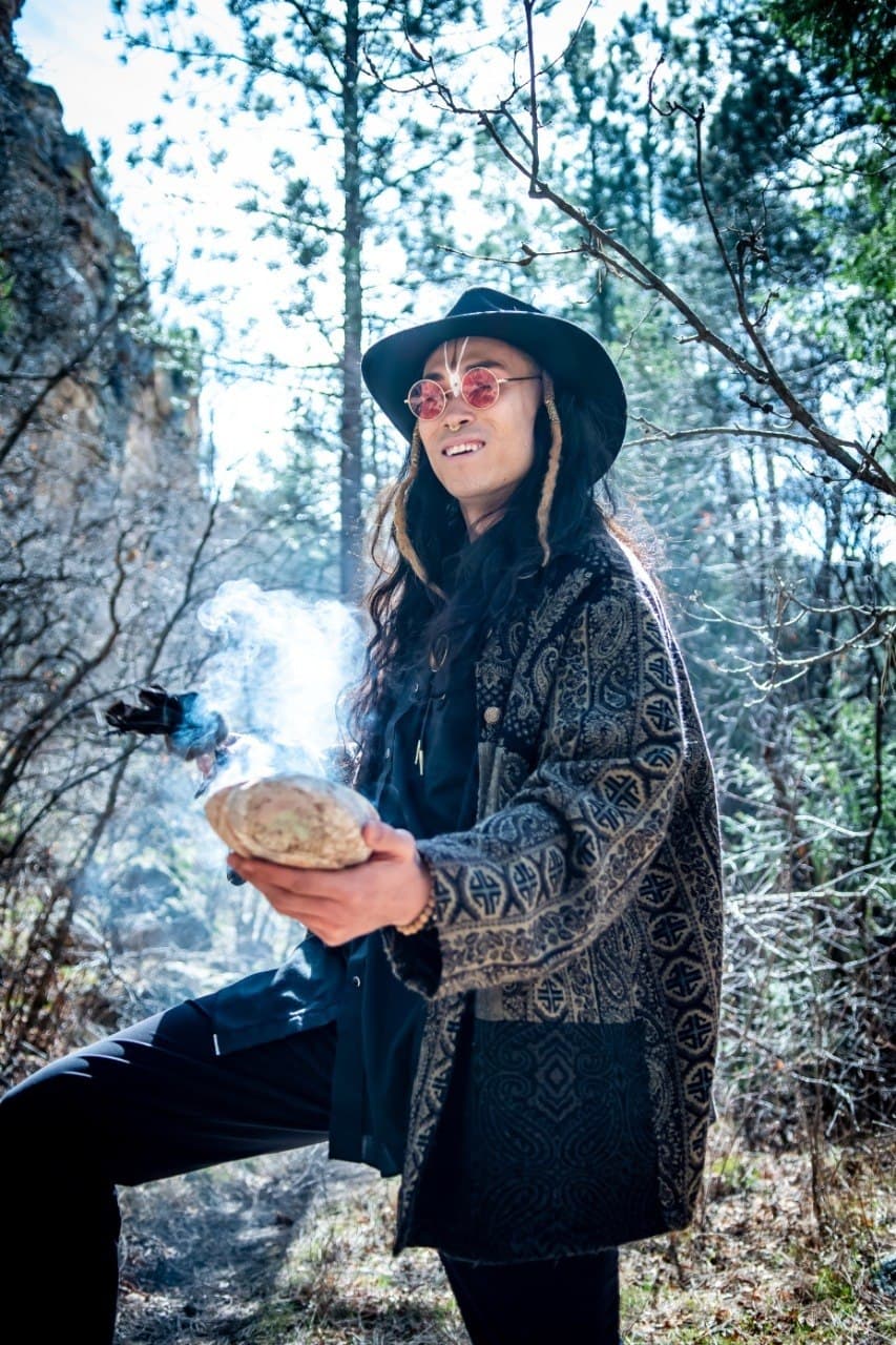 C Bliss holding a ceremonial bundle and sacred herbs in the forest